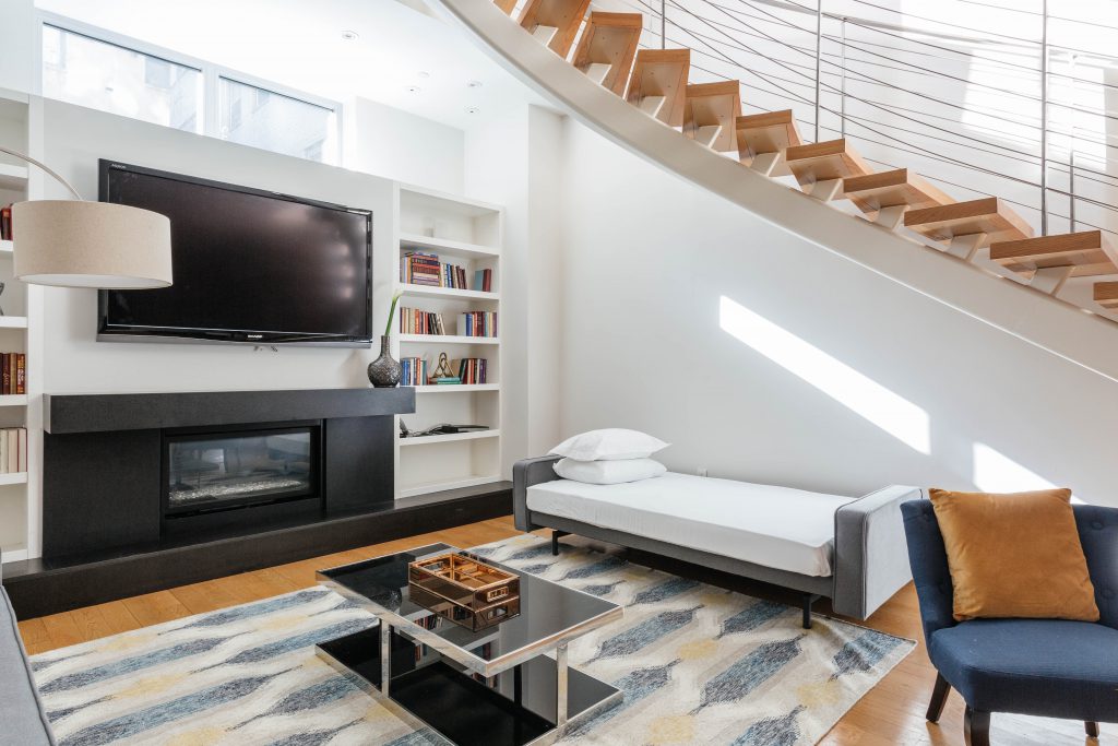 living room with sofa bed, coffee table, book shelf and curved stairs