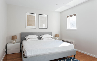 a newly furnished room with a bed, nightstands, and two framed paintings above the bed
