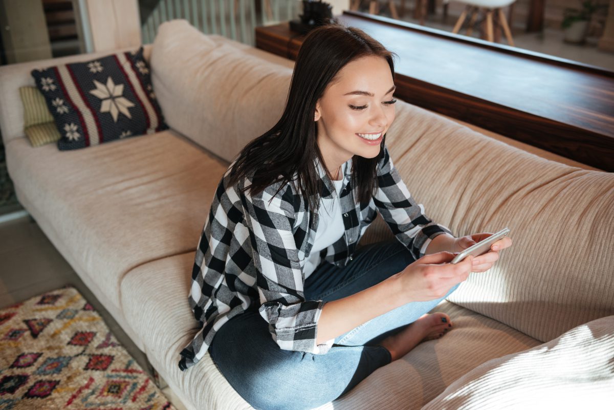 a woman sitting on a couch smiling at her phone