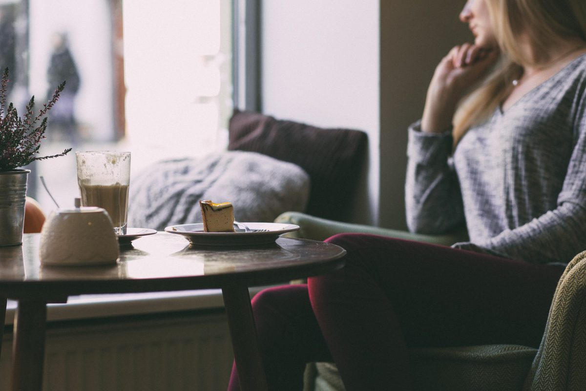  Une femme est assise à une table avec une tranche de gâteau à moitié mangée et regarde pensivement par la fenêtre 